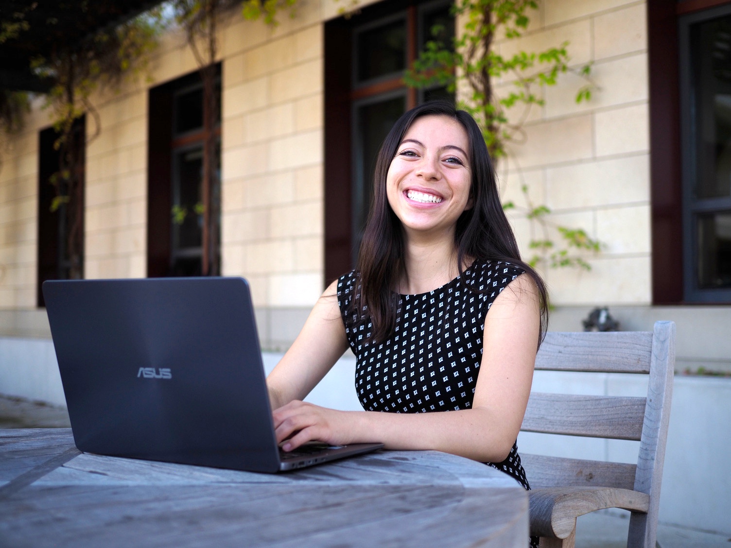Smiling woman working on laptop outside sunny office building