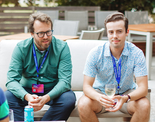 Two men sitting at an outdoor event with drinks Hertz Fellows